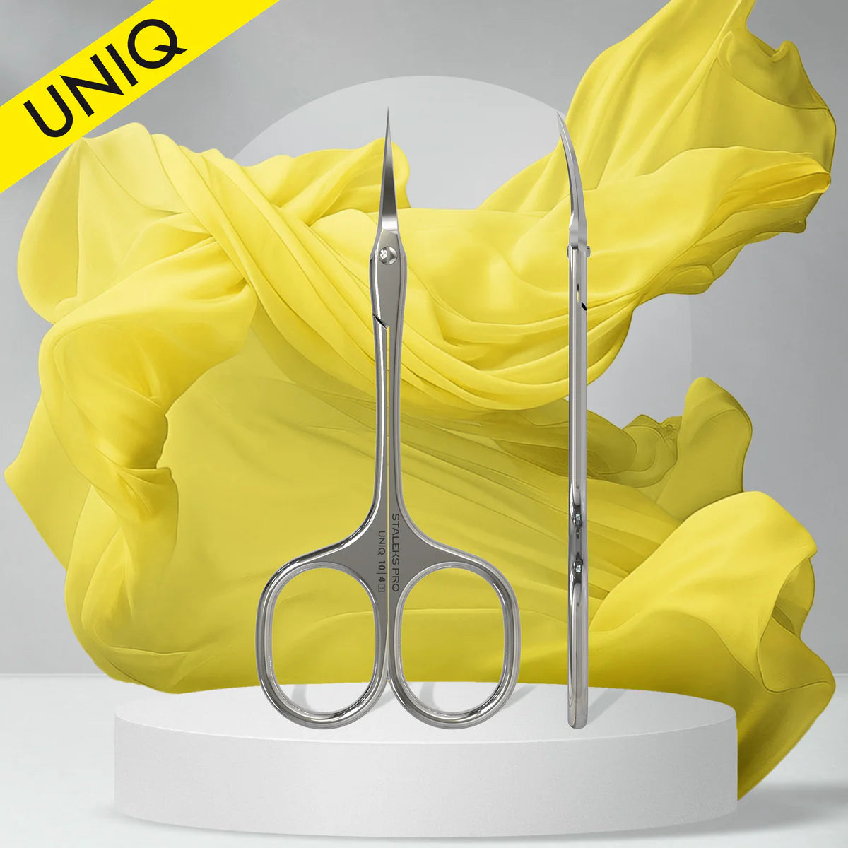 Professional Ballerina UNIQ 10 TYPE 4 cuticle scissors with stainless steel blades against flowing yellow fabric on white pedestal